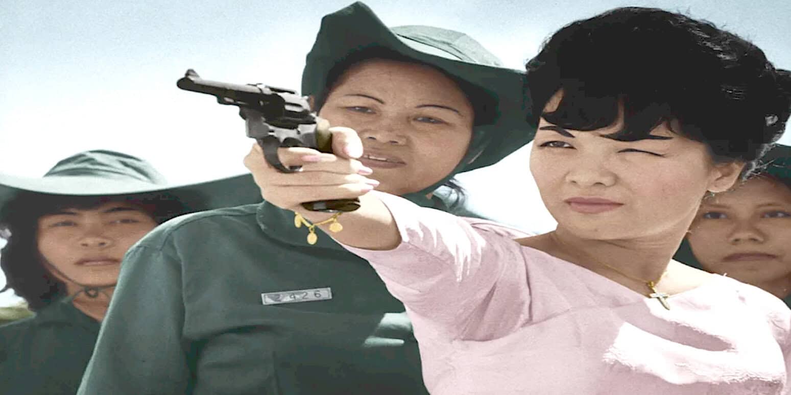 A woman in a military uniform aiming a pistol, surrounded by women in hats, representing a historical moment of women's roles in news, history, and music archives.