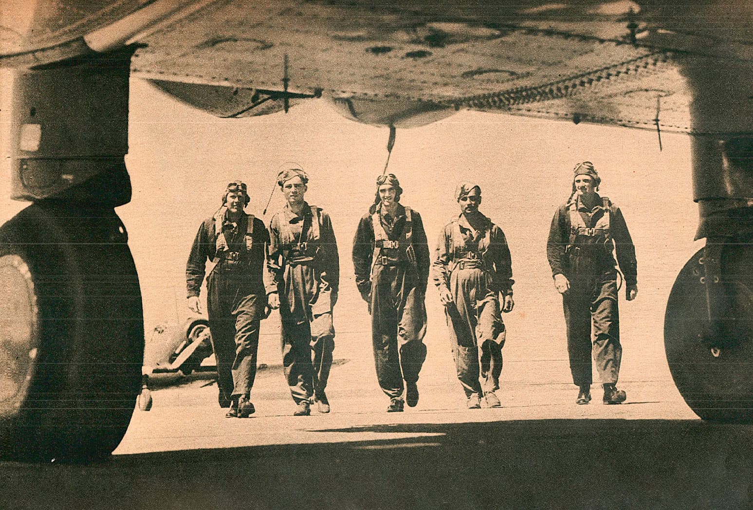 Vintage black and white photo of five female WWII pilots walking beneath a military aircraft on the tarmac, showcasing women in aviation and historic military aircraft.