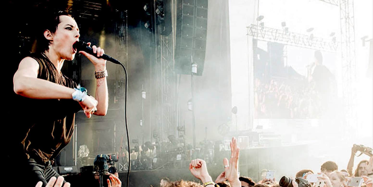 Female rock singer performing at music festival in front of crowd during outdoor concert at sunset, live music, music performance, festival scene.