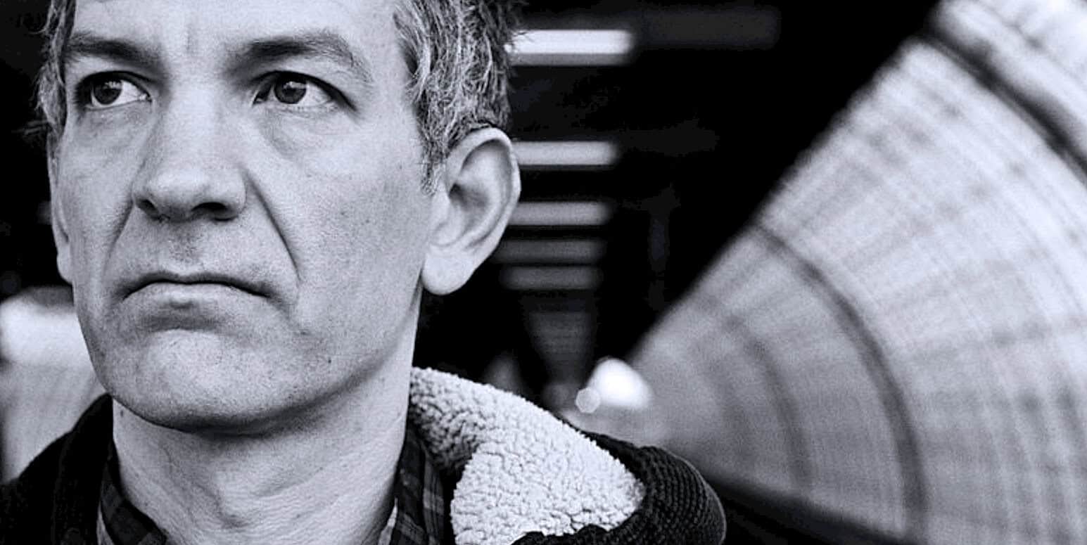 Close-up black and white portrait of a mature man with serious expression, emphasizing news, history, and music archives.