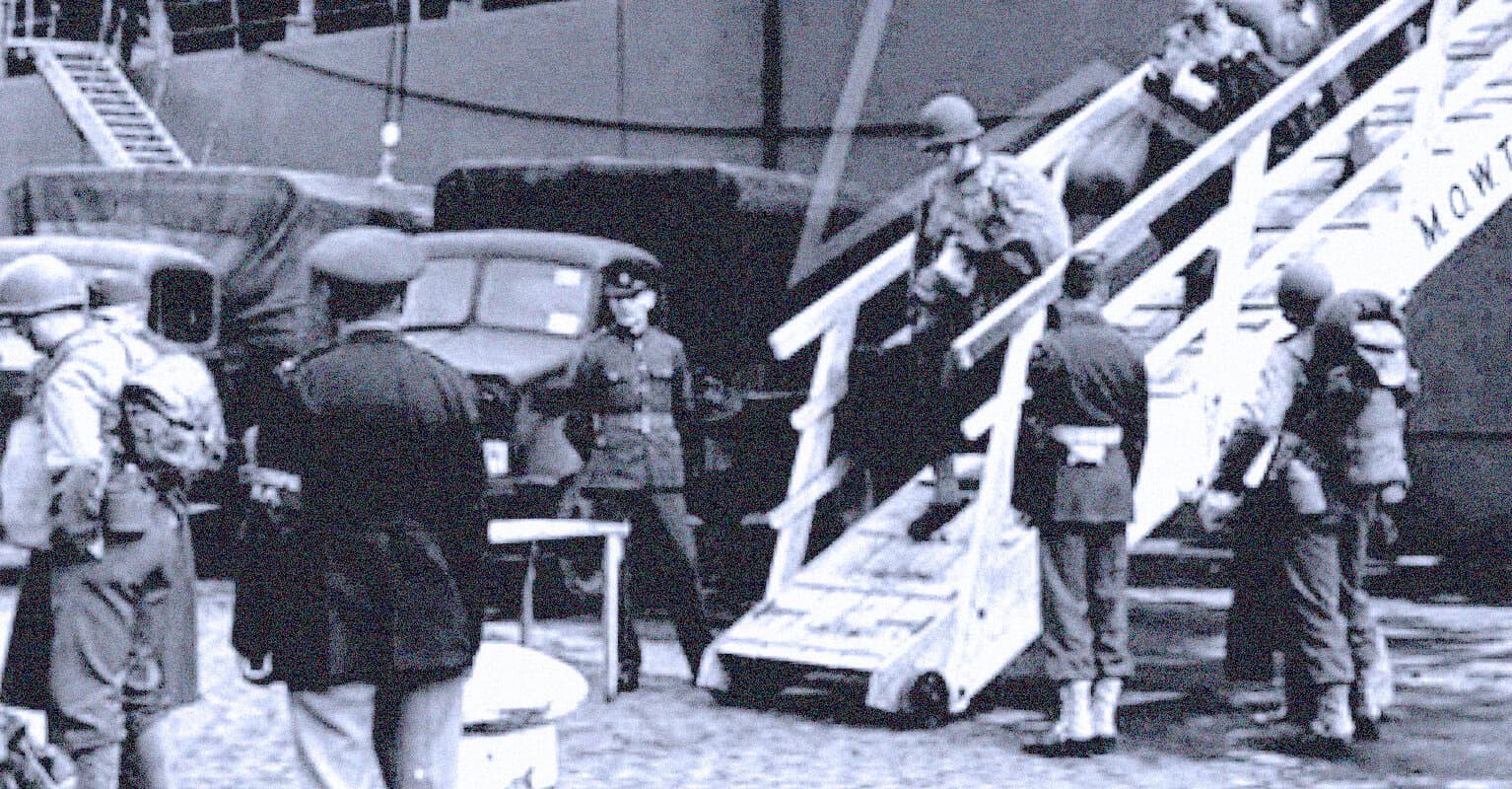 Military personnel boarding a transport aircraft during WWII, historic wartime photo, soldiers in uniform wearing helmets and face masks, army trucks and equipment in background, black and white image, military history, war archive.