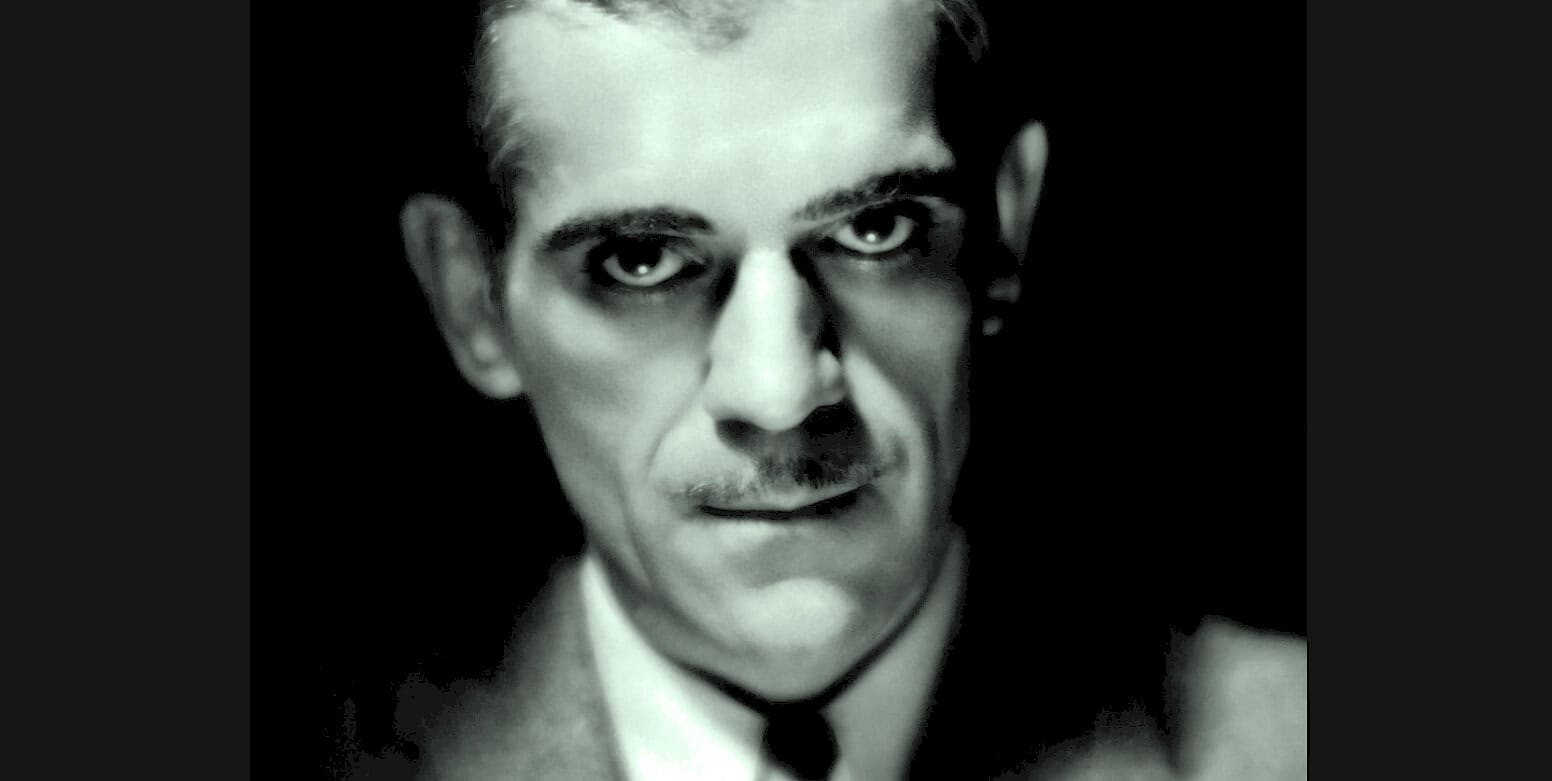 Close-up of a vintage black and white portrait of a man with intense eyes, suited formal attire, representing historical news, music, and history archive themes.