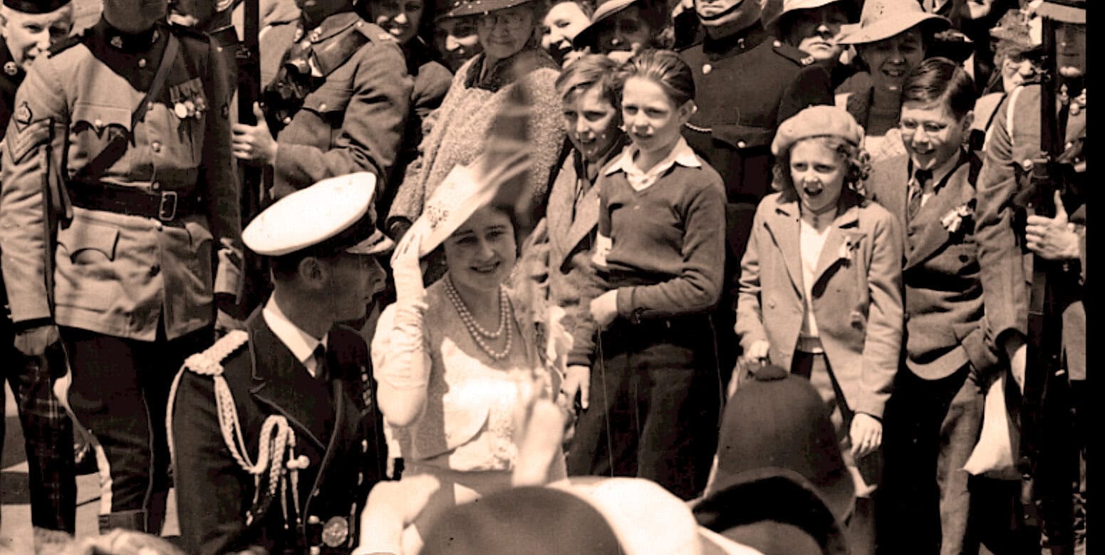 A black and white historical photo of civilians and military officers, including children, gathered outdoors during a wartime event, capturing moments of history and community life.