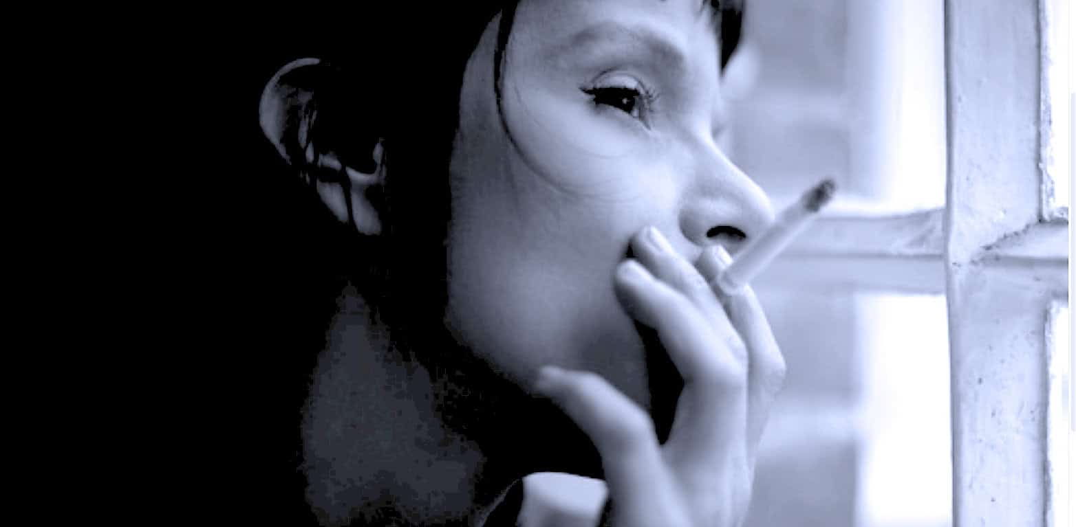 A woman smoking a cigarette, looking out a window, black and white photo, capturing a mood of nostalgia, contemplation, and vintage atmosphere, relating to music, history, and sound archives.