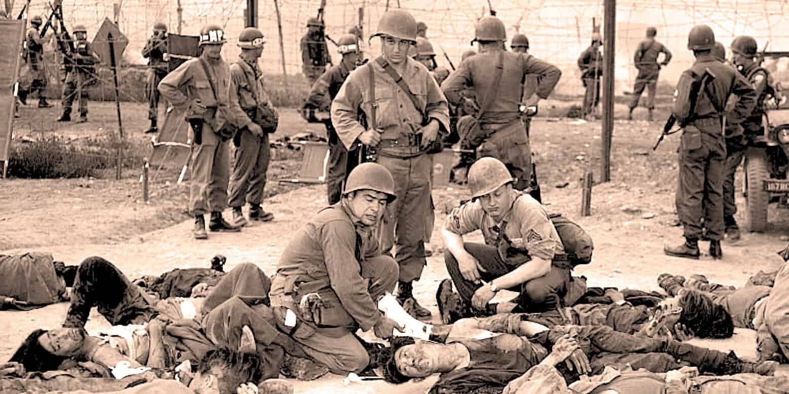Stacks of soldiers lying on the ground during the Vietnam War, with medics attending to the wounded and soldiers standing in the background, illustrating a historical war scene.