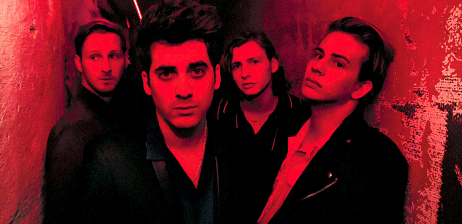 Vintage band photo with four young musicians, dark clothing, moody lighting, and red tinted atmosphere, representing classic rock or pop music. Ideal for music history, band profiles, and retro music archives.
