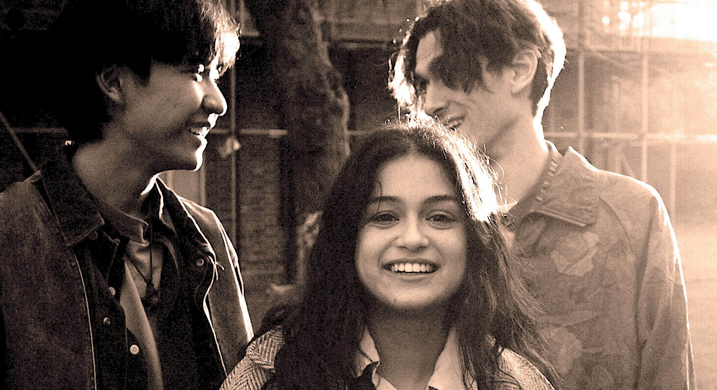 Smiling young woman with two men outdoors at sunset, vintage photo, music and cultural history, social gathering, joyful expression, casual clothing, late 20th century vibe, nostalgia, community, friendship, past daily archive relevance.