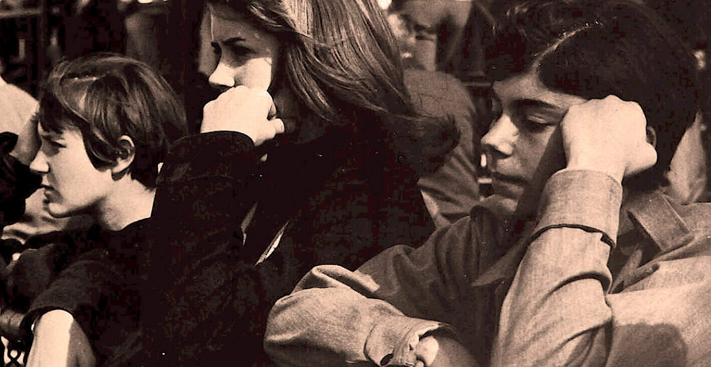 Seated young people listening to music at a vintage event, nostalgic black and white photo, retro concert or radio broadcast setting, music history, cultural moments, 1960s entertainment, vintage audience engagement, past daily sound archive relevance.
