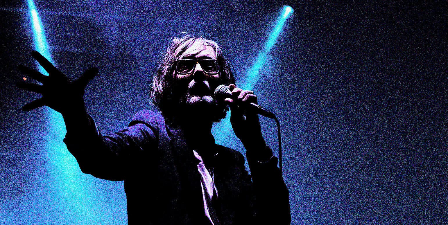 Vocalist performing on stage with microphone, dramatic blue lighting, live music concert, iconic performer, music nostalgia, historical music event, sound archive of news, history, and music.