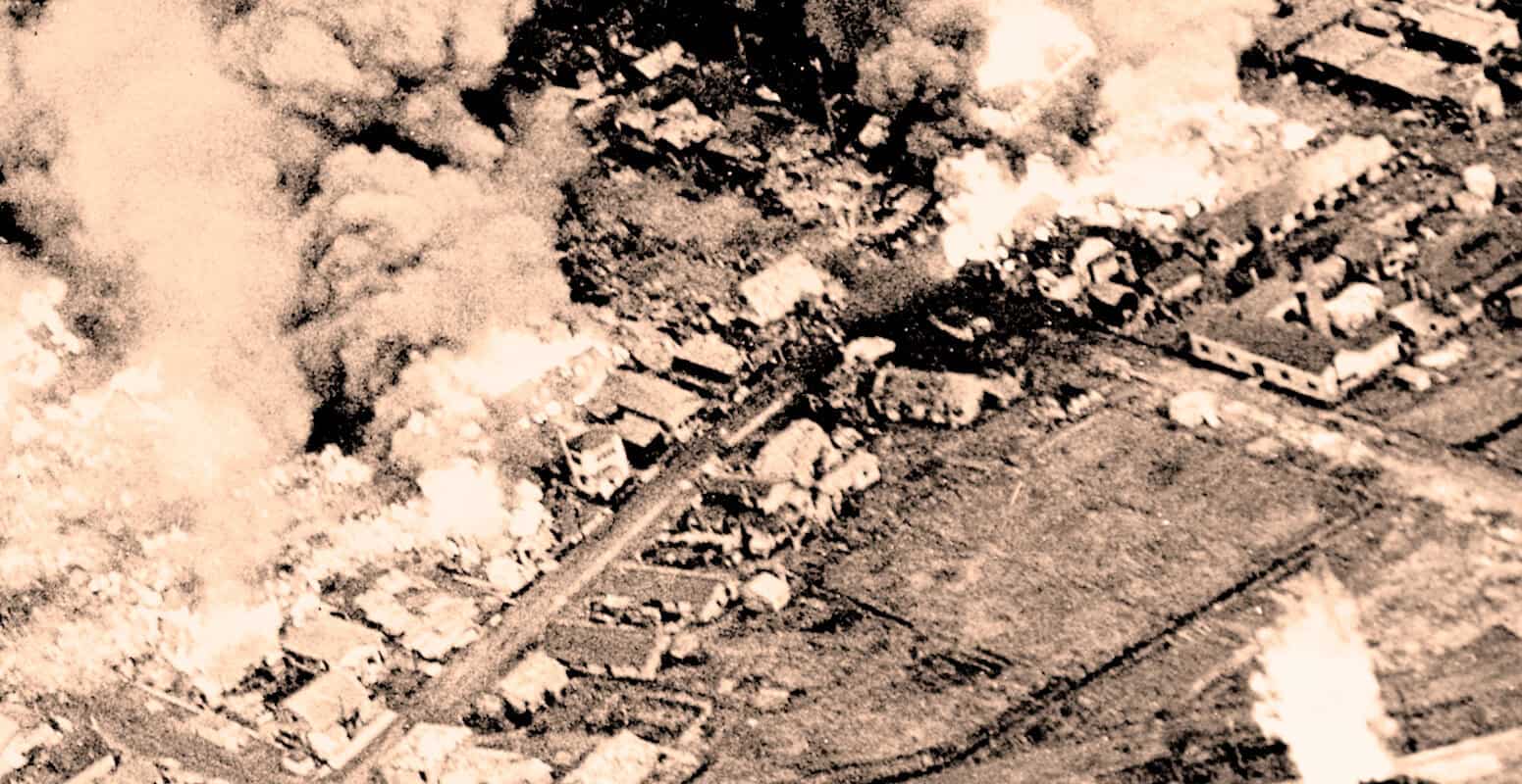 Bombing raid aerial view of city destruction during wartime, smoke rising from buildings and widespread devastation, historic photo illustrating wartime history and conflict.