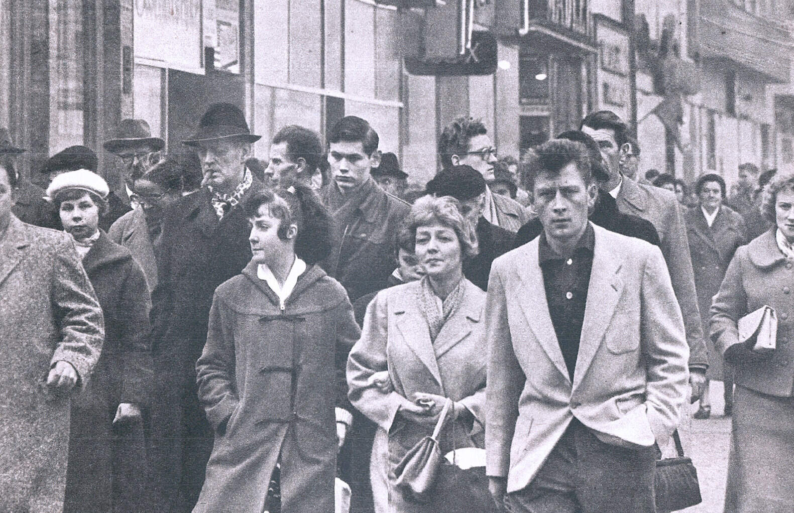 People walking on city street during daytime, vintage black and white photo, historic urban scene, street life, mid-20th century urban crowd, social history, daily life, black and white image.