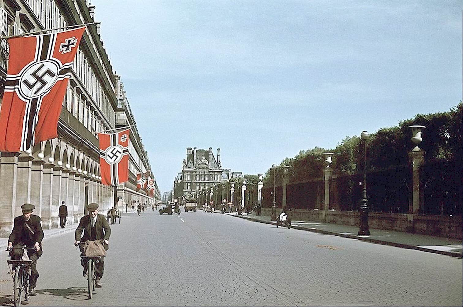 Banners with swastikas hanging on a historic European city street, symbolizing Nazi Germany era, with vintage bicycles and architecture, relating to historical news archives and World War II history.