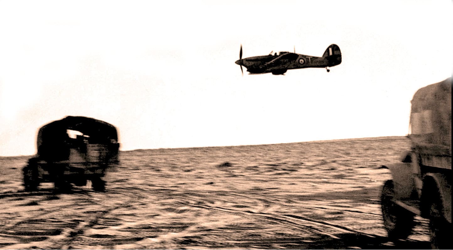 Aerial WWII fighter plane flying over a war-torn landscape with vehicles on the ground, historical war scene, vintage military aircraft, and battlefield setting.