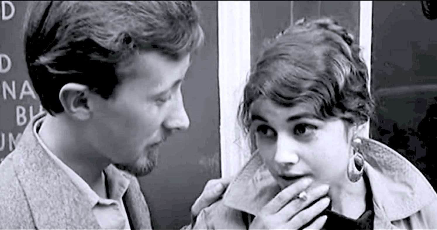 Old black and white image of a man and woman engaging in conversation, capturing a moment of interaction at a historical event or broadcast.