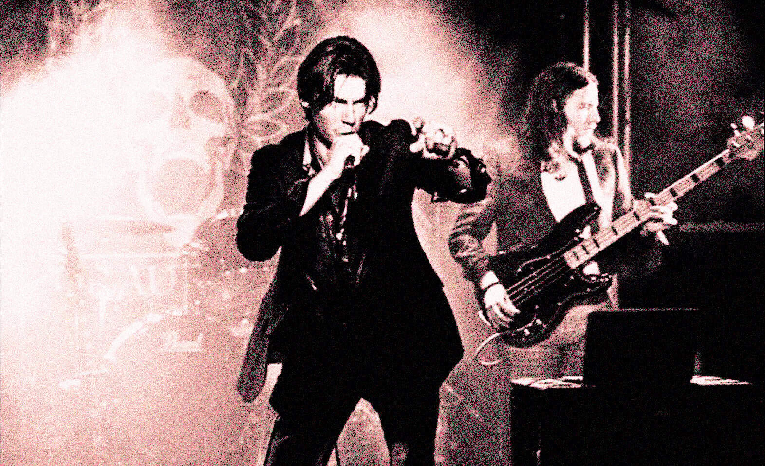 Vintage black and white photo of a musical band performing live, featuring a male singer and a female bassist, captured during a concert emphasizing music history and classic rock.