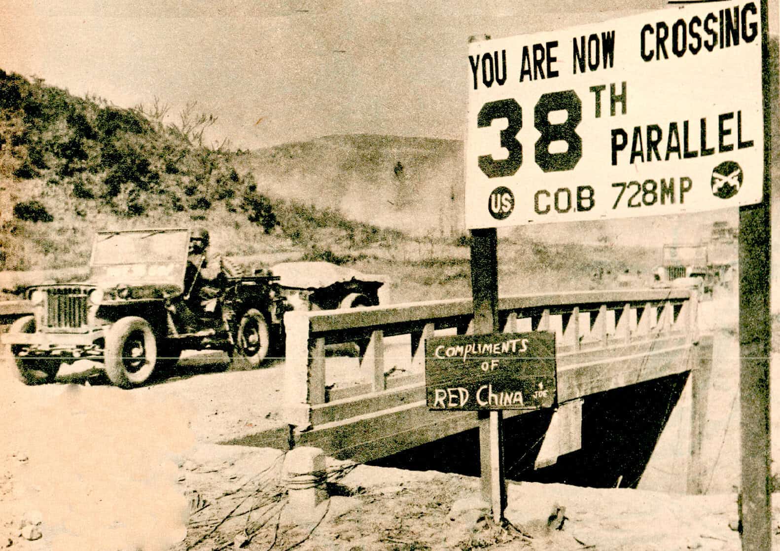 Vintage black and white photo of a crossing sign on a bridge, highlighting the 38th parallel border between North and South Korea, with an old military vehicle in the background.