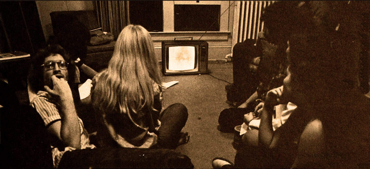 Watching a vintage television broadcast in a cozy, dimly-lit living room, with people gathered around, highlighting historical media, radio, and TV archive collections.