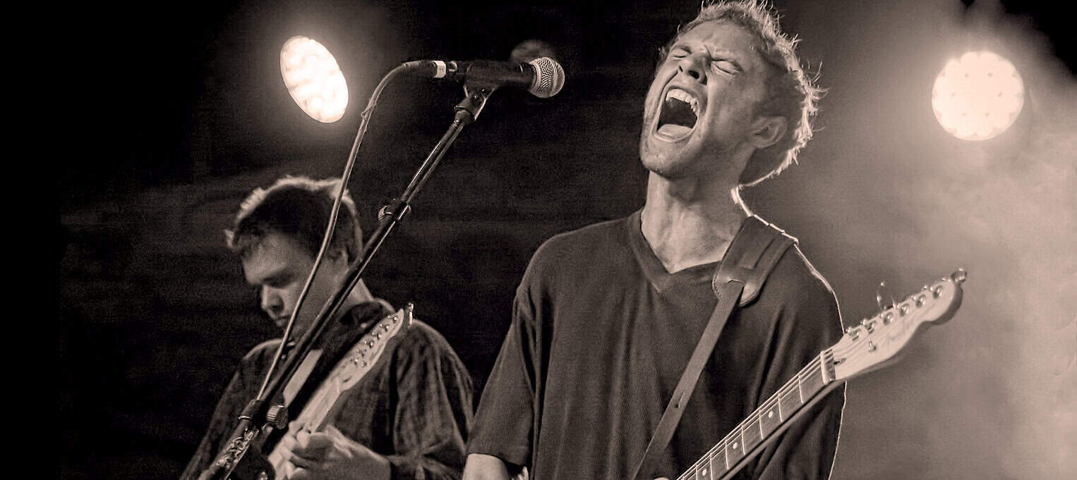 Film image of a singer and guitarist performing with passion on stage at a live music event, capturing raw emotion and energy, black-and-white photo emphasizing musical intensity and classic rock concert vibe.