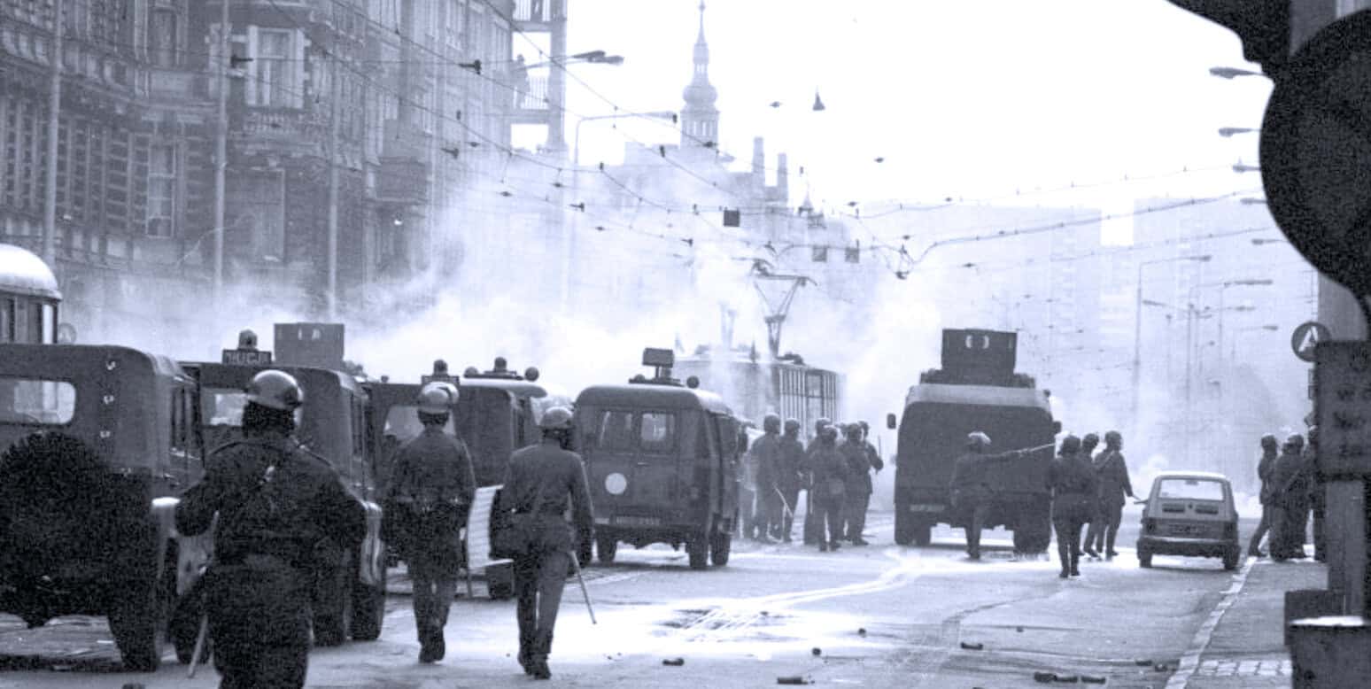 Protest or riot scene with police vehicles and protesters on city streets during a historic demonstration.