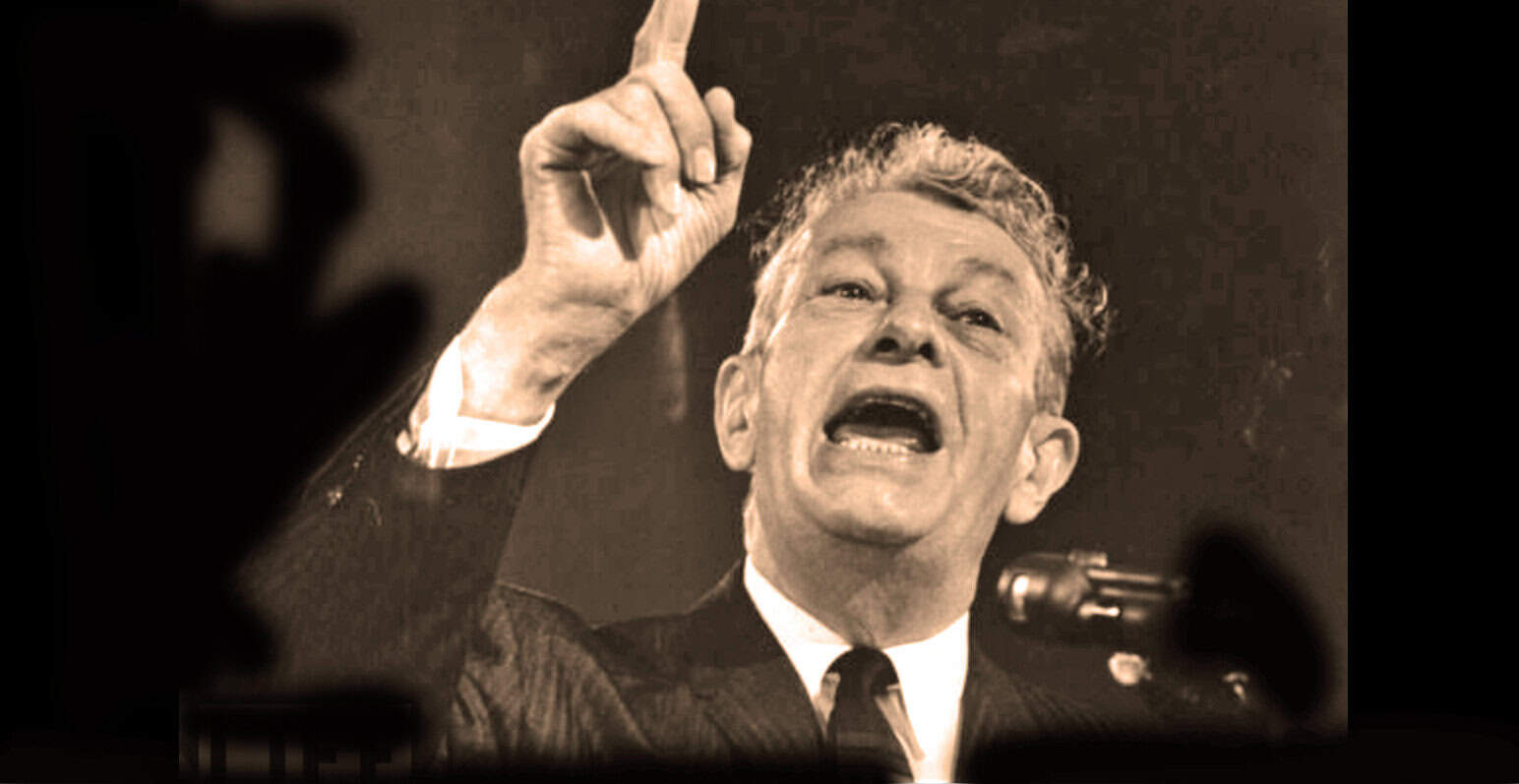 Historical black and white photo of a man speaking passionately at a press conference or rally, emphasizing speech and political activism, with a raised finger, symbolizing leadership and historical moments in news and history archives.
