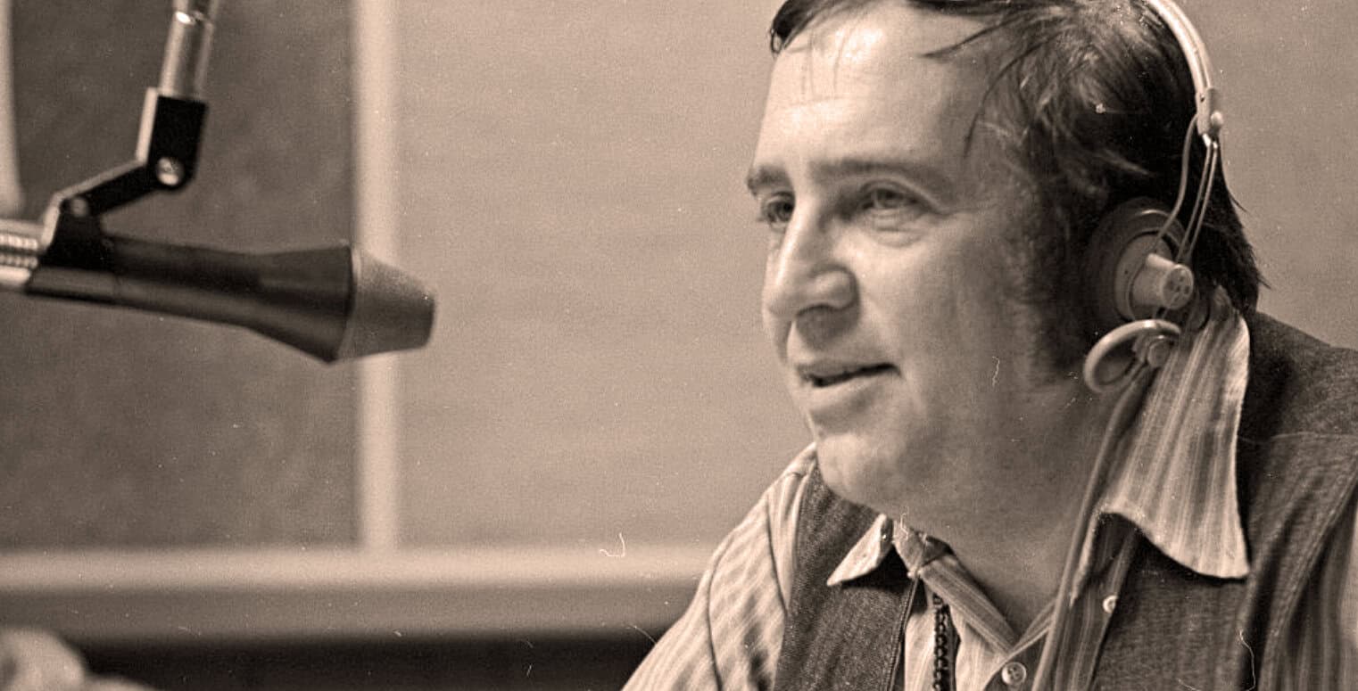 A vintage black-and-white photograph of a man in a radio studio wearing headphones and speaking into a microphone, capturing the essence of radio broadcasting, news, history, and music archives.