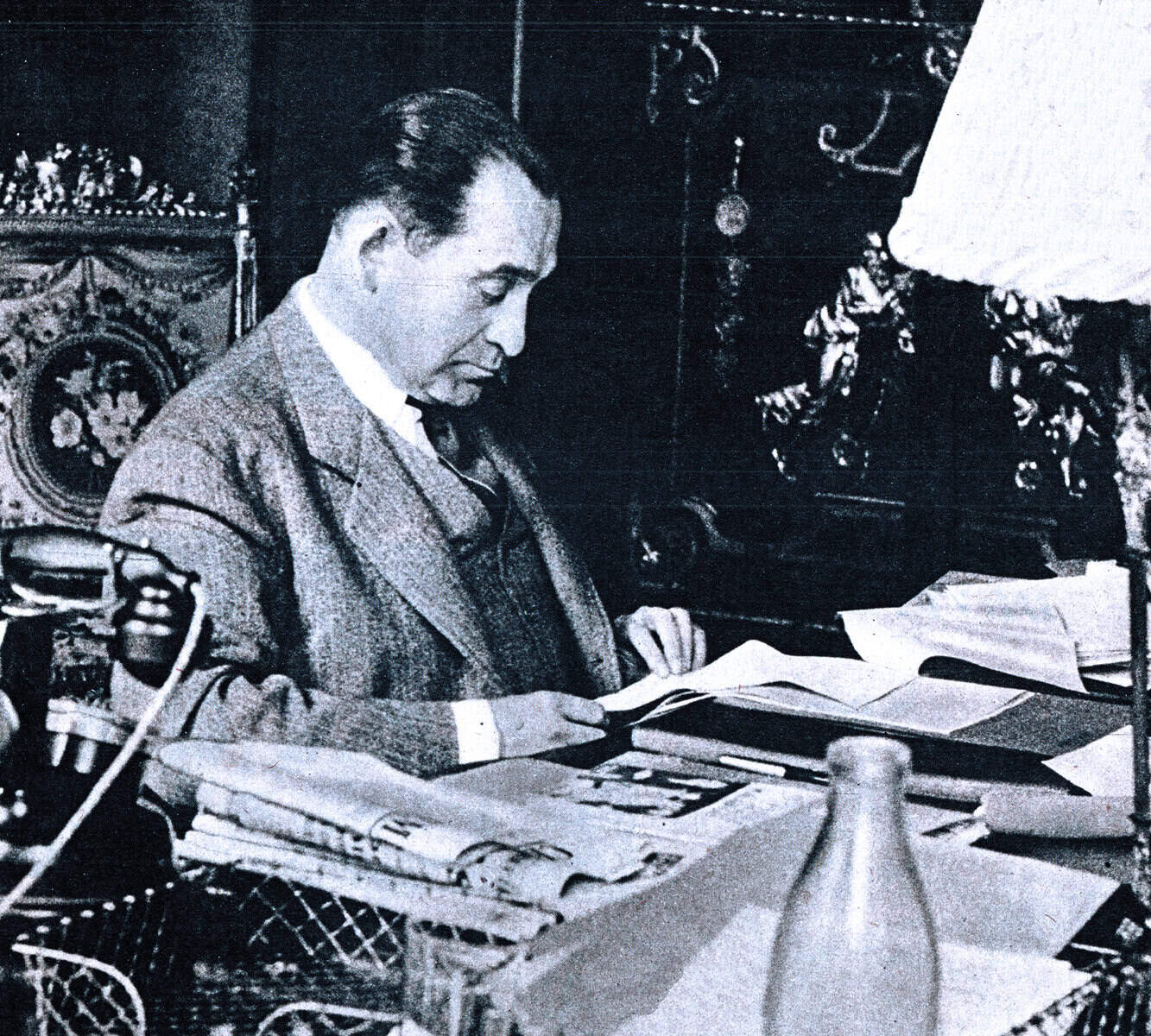 Vintage black and white photo of a man reading documents at a cluttered desk, capturing a historical moment related to news archive, music, and history from Past Daily.