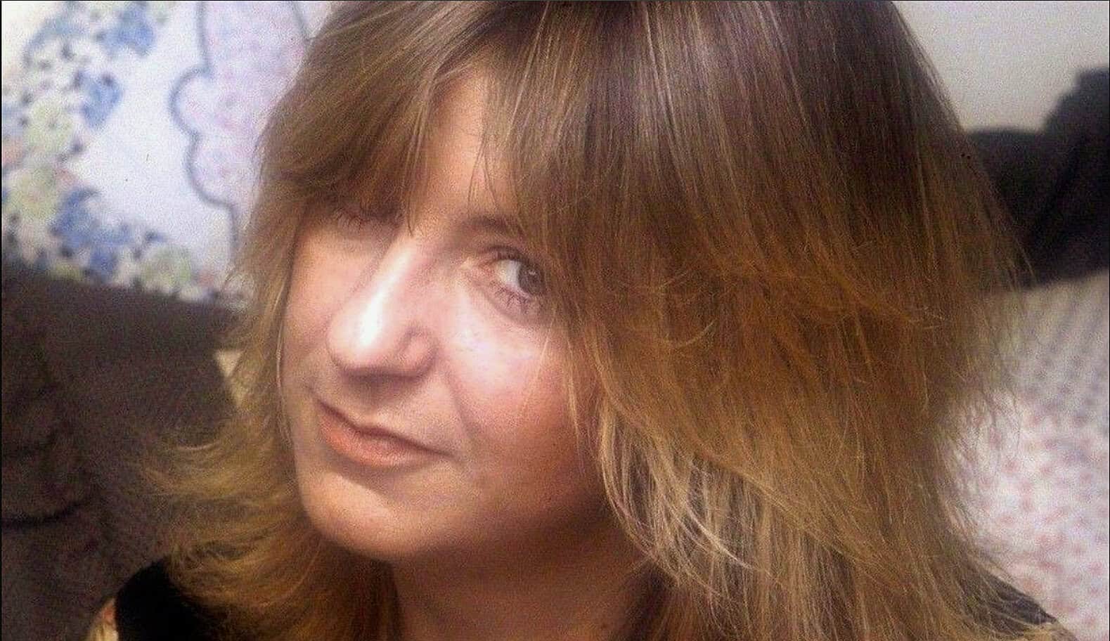 Vintage woman with long brown hair, featuring classic 1970s style, smiling and winking in a candid photo related to news, history, and music archives.