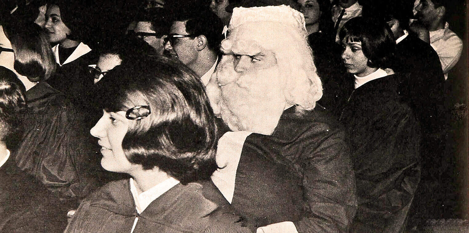 Silent film with a man in white wig and black attire among a diverse group of students attending a lecture or presentation, capturing an educational and historical moment for archive.