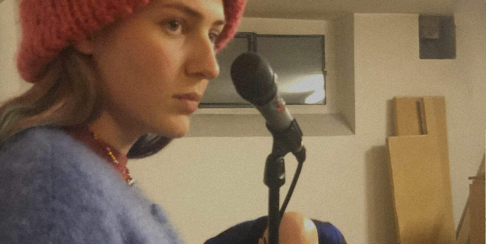 A woman with a red beanie speaking into a microphone in a recording studio for news, music, and history archives.