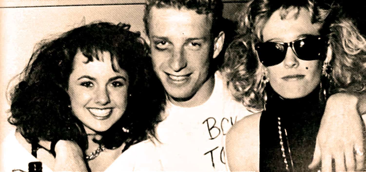 Vintage black and white photo of two vibrant women and a man, showcasing 1980s fashion with big hair, sunglasses, and accessories, representing music and pop culture from the era.