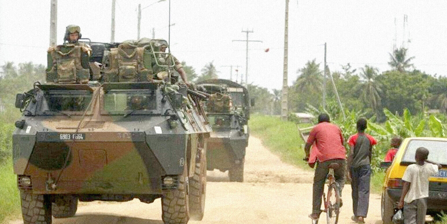 Military armored vehicle on a rural road with civilians and a cyclist nearby, illustrating conflict or warfare in a news and history context.