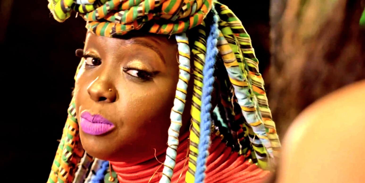 Vibrant woman with colorful braided headwrap and bold makeup, exploring cultural fashion and music themes with a focus on African heritage and artistic expression.