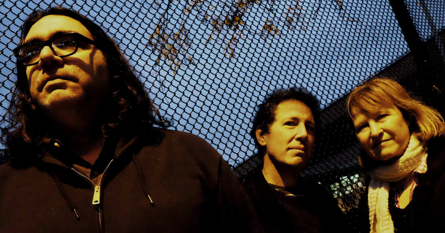 People standing in front of chain-link fence at dusk, urban music band, Alternative rock, live performance, musical artists, Past Daily news archive, history, radio, music preservation, sound archive, historic music moments.