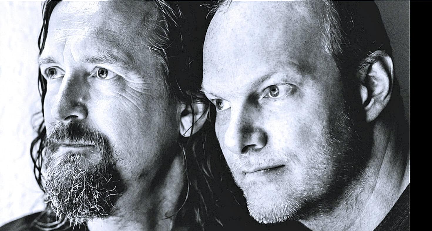 Close-up black and white image of two men with intense expressions, showcasing detailed facial features, representing historical news, music, and sound archive content from Past Daily.