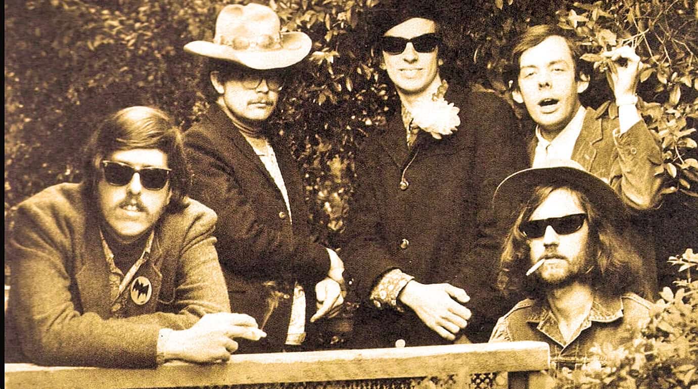 Vintage photograph of The Doors band members outdoors, wearing sunglasses and casual attire, capturing a moment of their iconic rock era.
