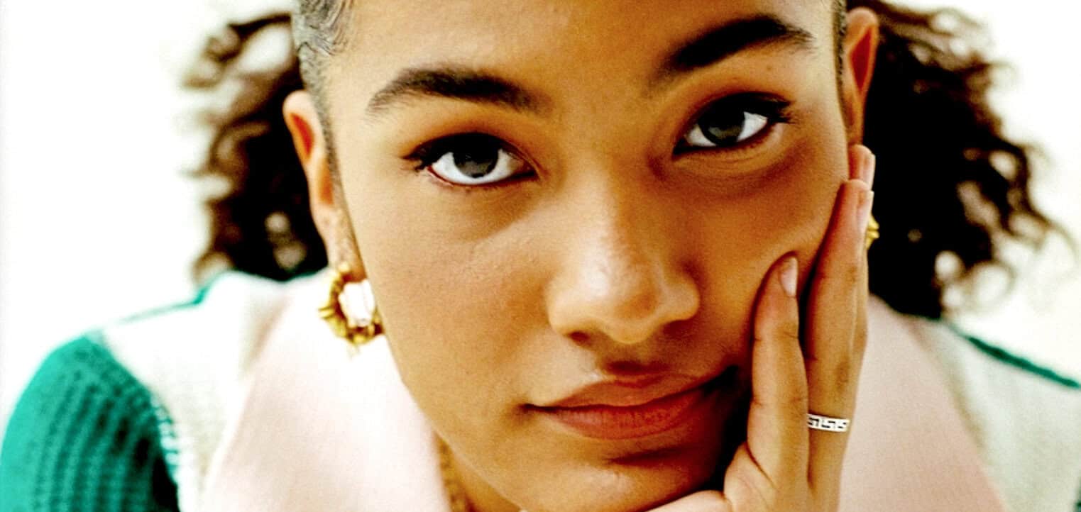 Close-up portrait of a young woman with expressive eyes, gold jewelry, and curly hair, illustrating the themes of news, history, and music archives featured on Past Daily.
