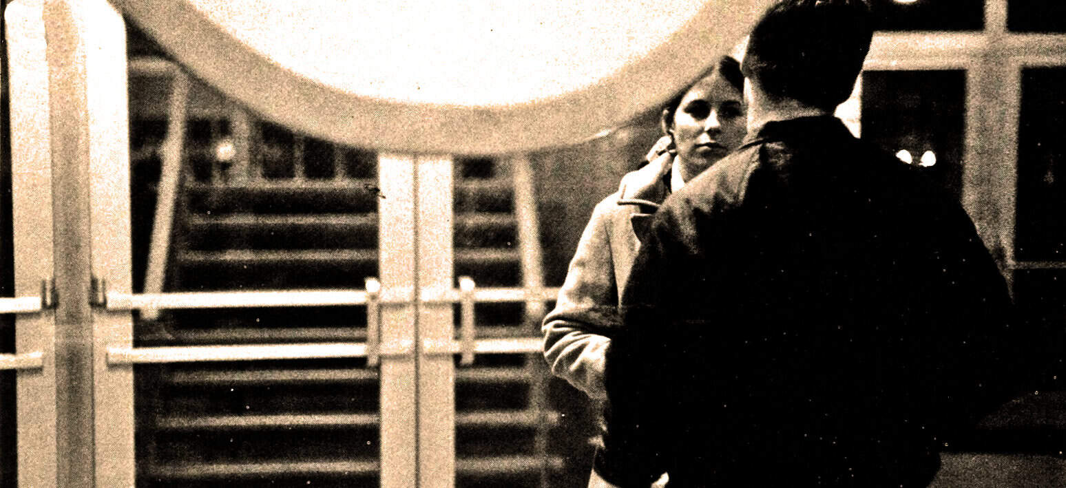 Vintage black and white photo of a man and woman having a conversation on a city street at night, capturing city life, human interaction, and historical urban moments.