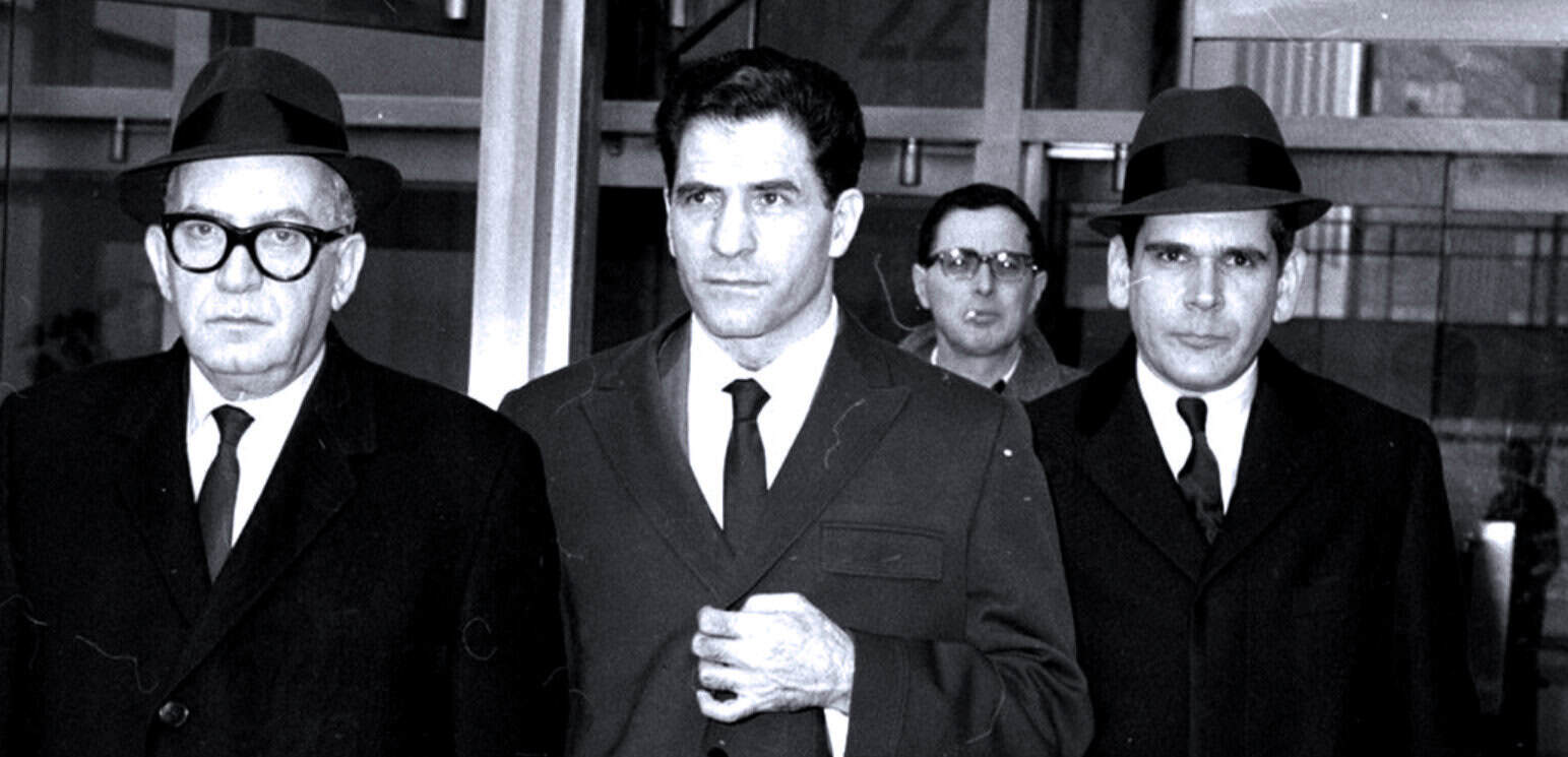 Black and white historical photo of four men in suits and hats, possibly from the 1950s or 1960s, walking in an indoor setting; vintage music and news archive featuring mid-20th-century figures.