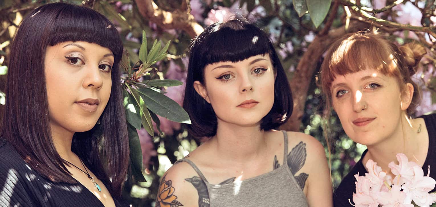 Women with tattoos and alternative style outdoors among flowering bushes, representing modern cultural diversity and music scene; best for news, history, and music archives.