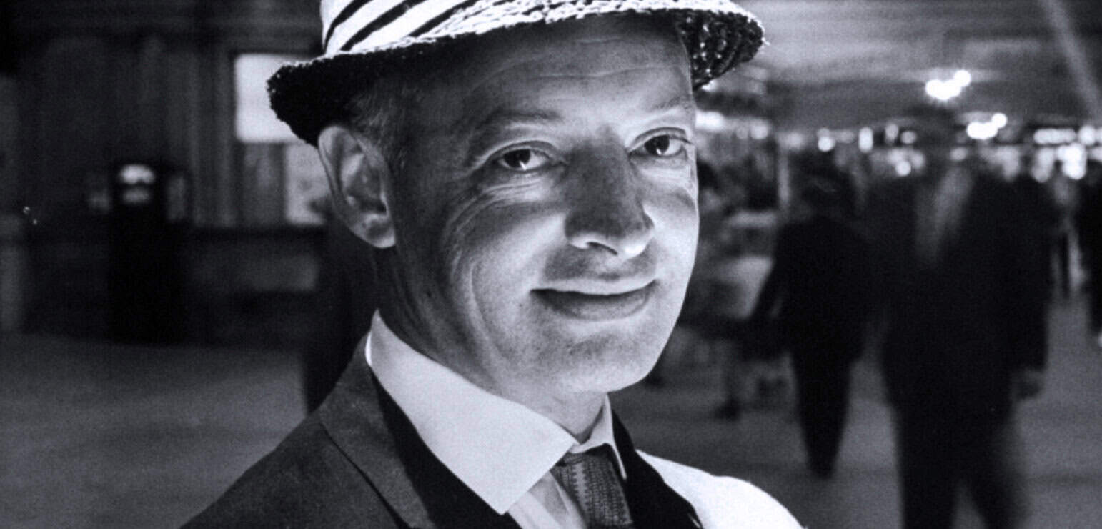 Portrait of a smiling man wearing a fedora hat, vintage style, in black and white, capturing a nostalgic moment related to news history, music, and archival media on Past Daily.