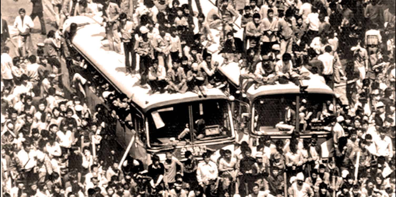 Crowd of people gathered around buses during a historical event, reflecting news coverage and social gathering in the past.