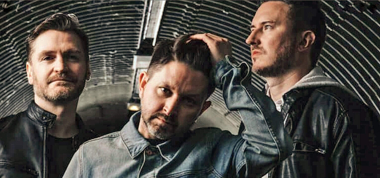 A black and white photo of three men in leather jackets posing in a tunnel, representing music and cultural history, showcasing a modern band or musical group with a vintage style.