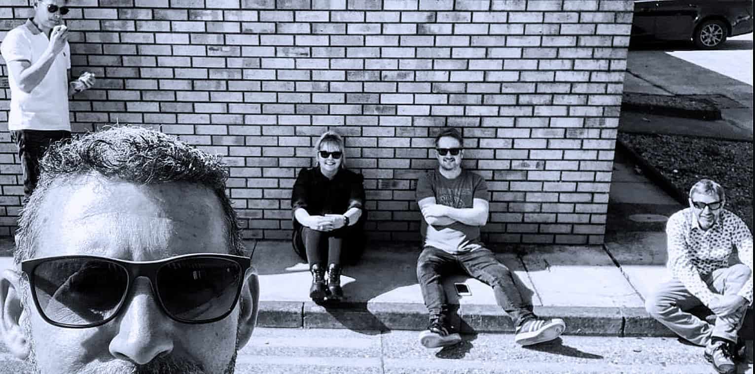 People sitting and standing outside on sidewalk in urban environment.