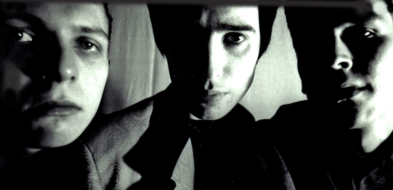 Young men portrait, black and white photo of three friends, casual style, moody lighting, alternative fashion, close-up shot, candid image, music band members, cultural expression, artistic photography, nostalgia, vintage vibe, classic rock inspiration, modern youth style, exploring identity, music history, American culture, social connection, Past Daily archive, news and music history, vintage music photographs.