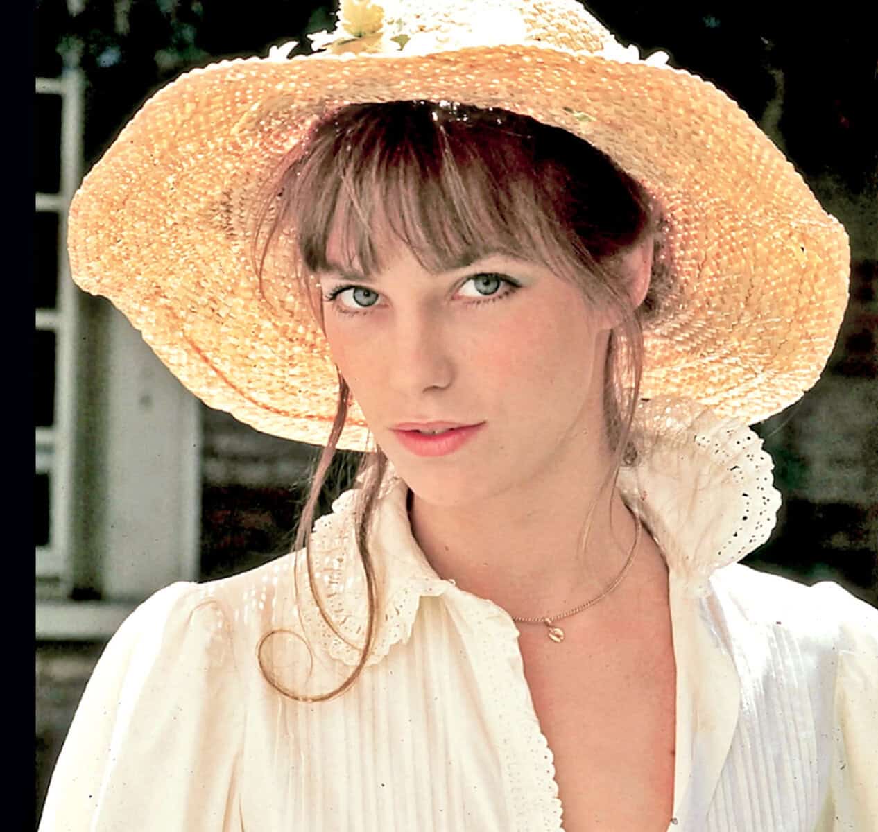 Vintage woman wearing a straw hat and white blouse, outdoors in a lush garden setting, capturing a nostalgic summer vibe and classic fashion style.