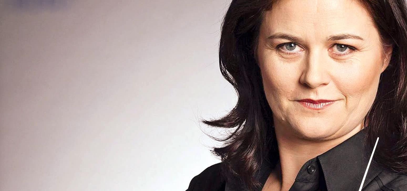 Close-up portrait of a confident woman with dark hair and blue eyes, representing a professional subject for news, history, and music sound archive content.