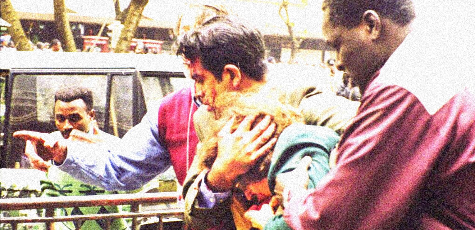 A man holding a dog while crowd safety officers intervene at a public event in an outdoor setting.