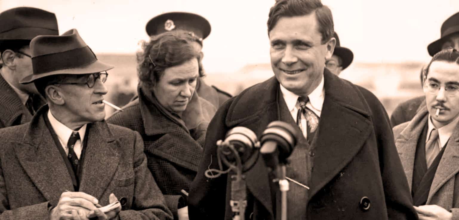 Historic news interview with a man smiling at microphones, World War II era, vintage photography, historical news archive, 1940s documentation of political figures, iconic wartime reporting, black-and-white photo of journalist and politician, classic press conference scene, historical media coverage, pastdaily news archive relevance.