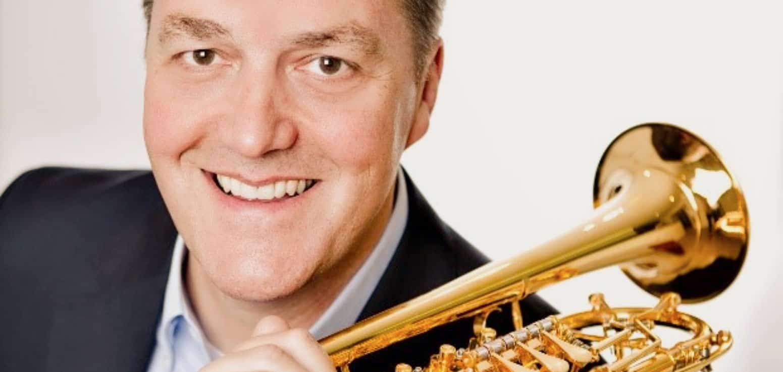Close-up of a smiling man holding a gold trumpet, emphasizing music and jazz themes for SEO.