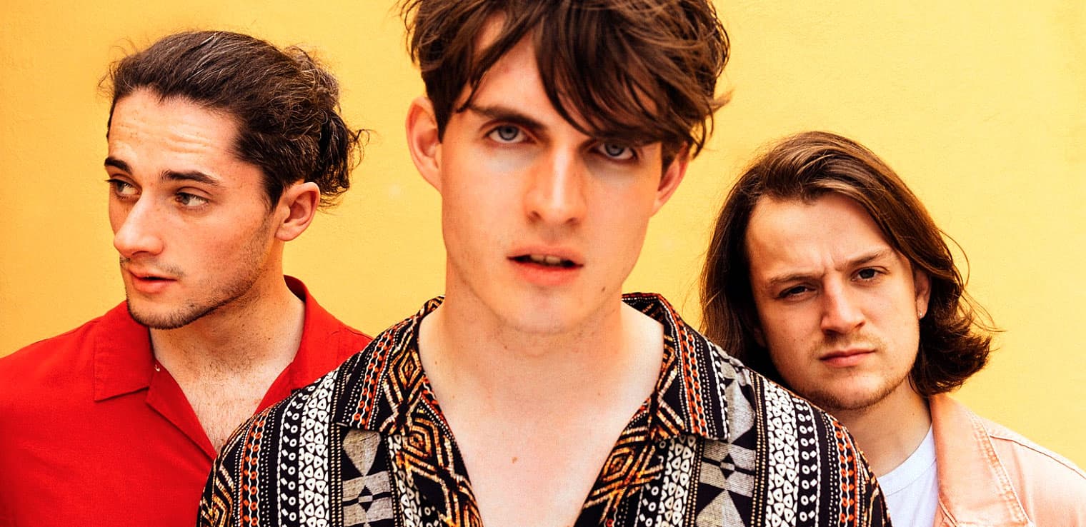 Young men with stylish hair and casual fashion posing against a yellow background, representing music and youth culture for SEO content.